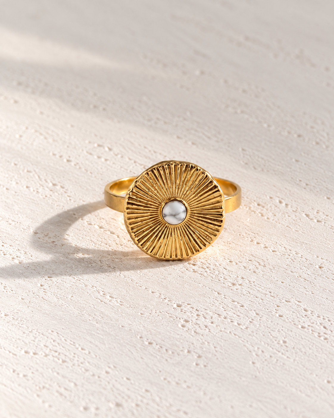 Anillo Soleil dorado tipo sol sobre cemento blanco