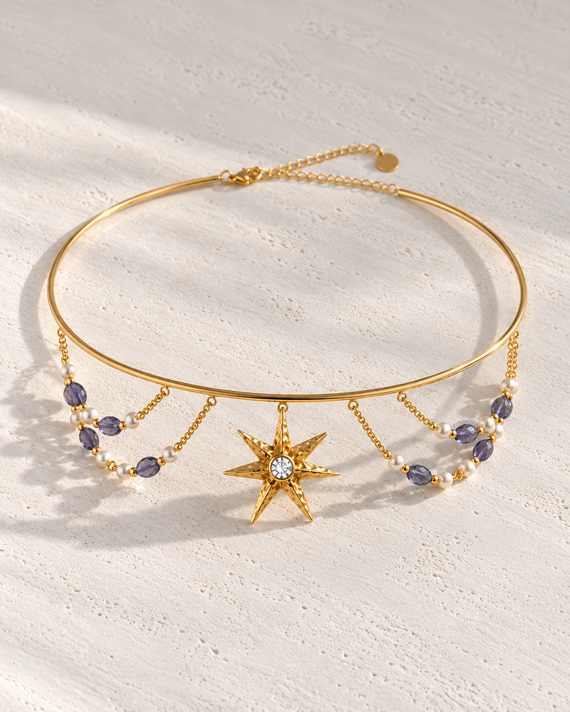 Choker Aurore dorado con estrella y perlas sobre cemento blanco