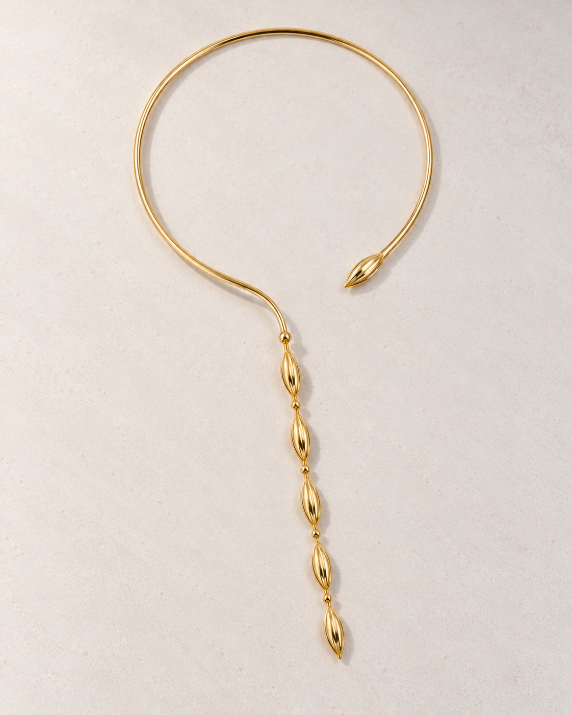 Collar Delphine rígido dorado con cuentas sobre cemento blanco